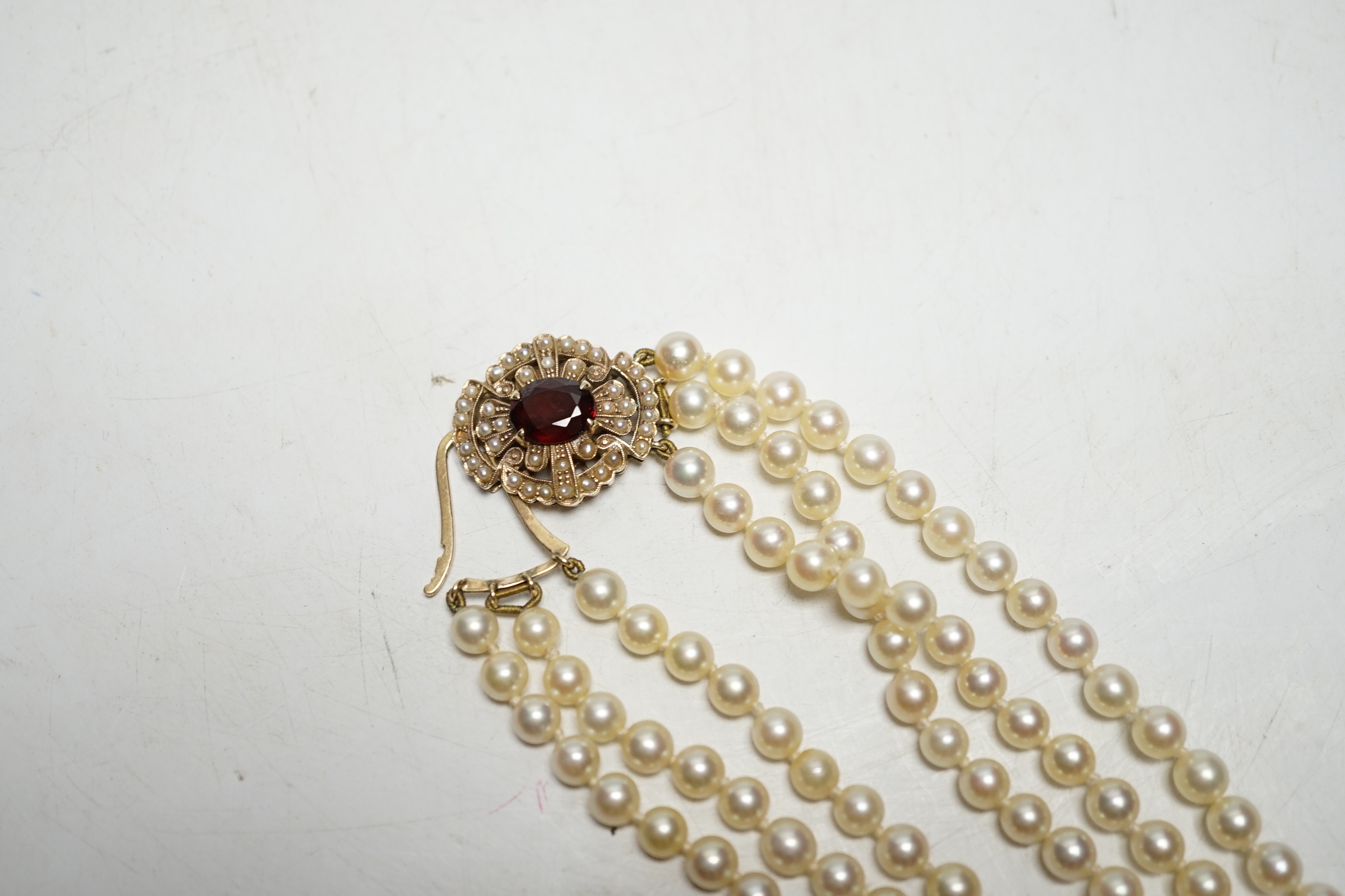 A 1960's triple strand cultured pearl necklace, by Cropp & Farr, with 9ct gold, garnet and seed pearl set clasp, 40cm.